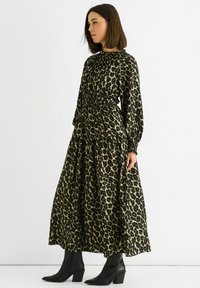 Maxi dress in a leopard print with elastic waistband, long sleeves, and a high collar. Paired with black heeled ankle boots.