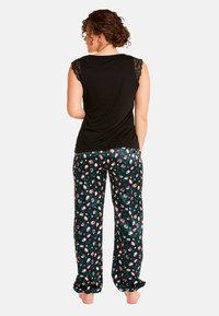 Haut sans manches noir avec des détails en dentelle, associé à un pantalon noir à motifs floraux dans des nuances de rose et de vert, en tissu ample.