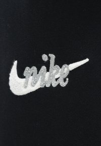 Črno blago z vezenim logotipom Nike; ima belo kljukico in sive napise, prikazuje teksturiran zaključek in čiste linije.