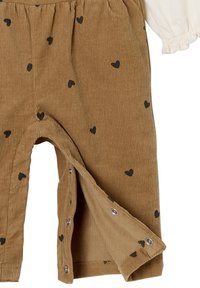 Braune Cord-Hosen mit kleinen schwarzen Herzmustern, ausgestattet mit Druckknopfverschluss an den Seiten und einem strukturierten Rippdesign.