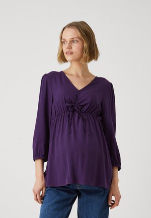 Top leggero viola con scollatura a V e coulisse in vita. Maniche lunghe e volumetrate con texture liscia, abbinato a jeans di denim blu.