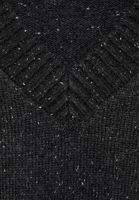 Schwarzer Strickstoff mit einem strukturierten Muster und helleren Sprenkeln. Das Design umfasst gerippte Details am Ausschnitt für zusätzliche Tiefe.