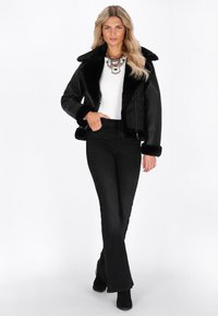Giacca in finta pelle nera con un colletto e polsini pelosi, abbinata a una maglietta bianca e jeans neri a zampa, accentuata da una collana d'effetto.