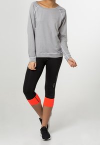 Sudadera atlética de manga larga gris claro con costuras blancas, combinada con leggings capri negros con acentos naranja brillante y detalles reflectantes.