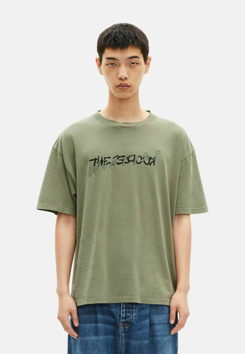 Εξ oversized ελαιοπράσινη μπλούζα με στρογγυλή λαιμόκοψη και κοντά μανίκια, προσαρμοσμένη με μαύρη στυλιζαρισμένη εκτύπωση στο μπροστινό μέρος. Φθαρμένη υφή.