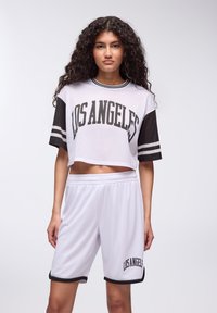 Top corto in rete bianco e pantaloni corti, entrambi con dettagli neri. Il top presenta "LOS ANGELES" in carattere grassetto, mentre i pantaloni corto hanno un dettaglio testuale abbinato.