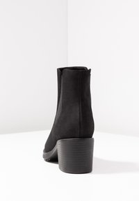 Botas de tobillo negras hechas de ante suave, con un tacón ancho y paneles laterales elásticos para ponerlas y quitarlas fácilmente. Textura lisa con un acabado mate.