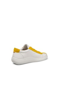 Vit sneaker med överdel i texturerad läder, gul mockadetaljer och en räfflad gummisula. Innehåller platta snören och en vadderad krage.