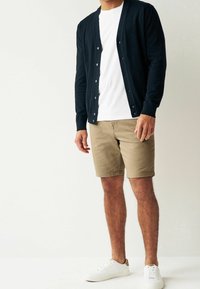 Cardigan bleu marine porté sur un t-shirt blanc, associé à un short kaki et des baskets blanches. Le cardigan présente une fermeture à boutons et des poignets côtelés.