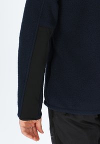 Giacca in fleece blu navy con corpo testurizzato e pannelli laterali neri lisci. Le maniche sono dotate di un dettaglio ai polsini, che migliora l'isolamento.