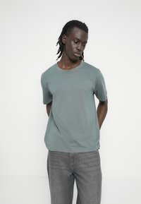 Κοντομάνικο t-shirt με στρογγυλή λαιμόκοψη σε απαλή απόχρωση μπλε-πρασίνου, κατασκευασμένο από απαλό βαμβακερό ύφασμα. Κανονική γραμμή με ελάχιστες ραφές και καθαρό σχεδιασμό.