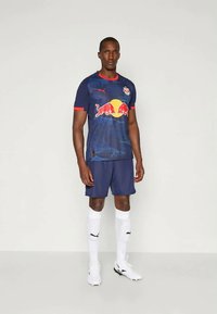 Námornícky športový dres s červenými akcentmi, zdobený grafickým potlačou a logom, spárovaný s pasujúcimi šortkami a bielymi ponožkami po kolená.