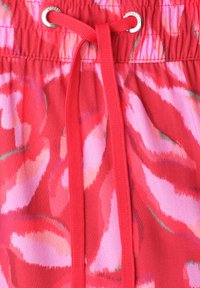 Tissu rouge et rose à motifs avec un cordon rouge noué passé à travers des œillets argentés à la taille.