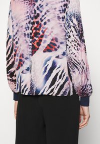 Translucent blouse with vibrant animal print in pink, purple, and red hues. Features balloon sleeves and fitted cuffs.