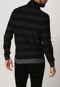 Czarny sweter w paski z wysokim kołnierzem, wykonany z miękkiego materiału. Posiada prążkowane wykończenia na dole i mankietach, prezentując luźny krój.