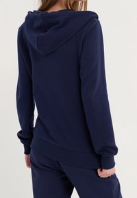 Sudadera con capucha azul marino hecha de una suave mezcla de algodón, con un bolsillo tipo canguro en la parte delantera, puños acanalados y capucha con cordón para un ajuste regulable.