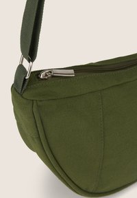 Borsa a spalla in canvas verde oliva con forma curvata, chiusura superiore con zip e superficie testurizzata. Presenta una tracolla regolabile e accessori in metallo.