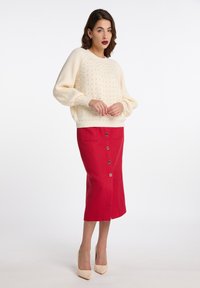 Pulover tricotat crema cu un model texturat si maneci cu tiv, asortat cu o fusta rosie, pana la genunchi, cu nasturi pe fata si buzunare laterale.