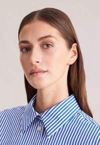 Camicia a righe blu e bianche con colletto classico e chiusura a bottoni, caratterizzata da una texture in cotone morbido e una vestibilità su misura.