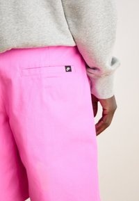 Pink shorts made of cotton, featuring a back pocket and a small black Nike logo tag. The fabric appears smooth with minimal texture.