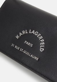 Black textured leather wallet featuring silver embossed text: "KARL LAGERFELD PARIS 21 RUE ST-GUILAUME." Compact rectangular shape.