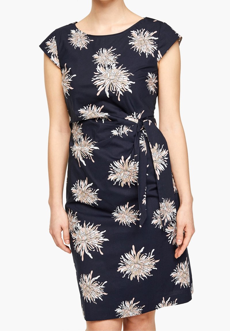 Robe bleu marine sans manches avec motifs floraux beiges et ceinture en tissu assortie à la taille.