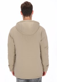 Chaqueta impermeable beige con capucha, con textura suave, detalles de costuras y puños ajustables. Diseñada para uso casual.