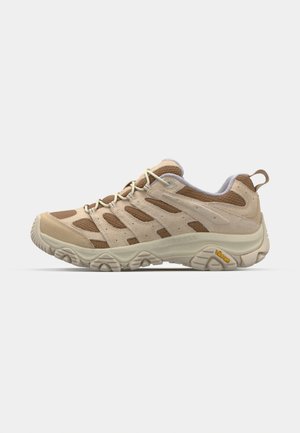 Chaussure de randonnée beige avec tige en mesh et suède, semelle en caoutchouc et système de laçage. Présente des panneaux texturés et le logo Vibram sur le côté.
