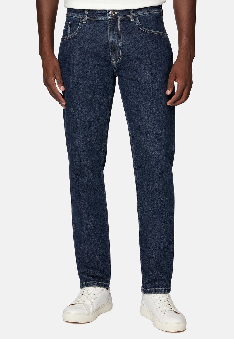 Temno modri kavbojki z ravnim krojem, zasnova s petimi žepi, subtilne šive, oblečeni z belimi supergami.