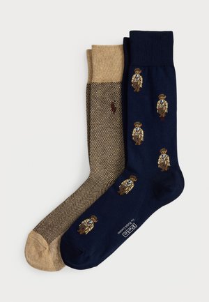 Two pairs of folded socks: one beige with a herringbone pattern and small horse logo, one navy with small vintage golfer illustrations.