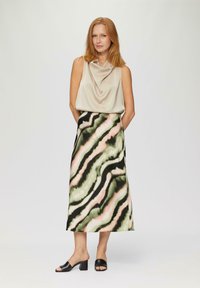 Bēšas krāsas cowl-neck tops, kas kombinēts ar garu rakstainu svārku zaļās, melnās un rozā krāsās. Izskatu noslēdz melni blokveida papēžu sandeļi.