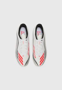 Witte sportieve schoenen met rode accenten en zwarte strepen. Beschikt over een gestroomlijnd ontwerp, vetersluiting en getextureerde zolen voor grip.