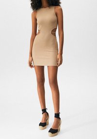 Vestido mini sin mangas en tono bronce con detalles recortados en los laterales. Combinado con cuñas de esparto negras con lazos en los tobillos y suelas de paja.
