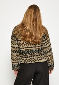 Mikina z fleece s výraznými hnedými, čiernymi a krémovými vzormi. Voľný strih, zaoblené plecia a mierne skrátený dizajn.