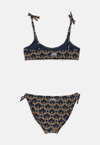 Σετ μπικίνι σε ναυτικό μπλε με σχέδιο από χρυσές αλυσίδες. Το πάνω μέρος έχει ρυθμιζόμενα λουριά και ετικέτα με λογότυπο· το κάτω μέρος διαθέτει δέσιμο στα πλαϊνά και συντονισμένο σχέδιο.