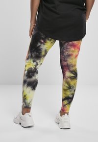 Flerfargede tie-dye tights har en blanding av gule, svarte og rosa nyanser. De er kombinert med hvite joggesko og en svart topp.