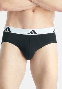 Schwarze Herrenunterhosen mit einem weißen elastischen Taillenbund, der mit schwarzen Adidas-Logo-Streifen versehen ist. Glattes Material und körperbetontes Design.