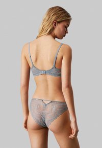 Set di lingerie grigio in pizzo con intricati motivi a onda, spalline regolabili e un delicato dettaglio a occhiello sul retro delle mutandine.