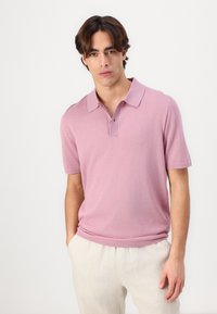 Polo triko v světle růžové barvě, krátké rukávy, zapínání na knoflíky, vyrobeno z hladké látky. Nosené neformálně s krémovými kalhotami.