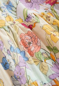 Un tessuto floreale in toni pastello presenta fiori rosa, blu, gialli e verdi con una texture morbida e una leggera lucentezza, che mette in mostra dettagli intricati.