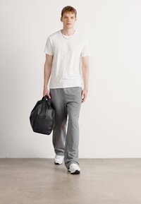 White short-sleeve t-shirt, gray sweatpants, and black leather bag. Model wears white sneakers and a silver chain necklace.