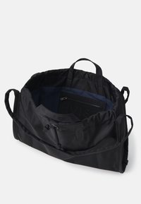 Schwarze Stofftasche mit weicher Textur, runder Form, zwei kurzen Griffen und Kordelzugverschluss. Das Innere ist mit einem marineblauen Futter und einer Reißverschlusstasche ausgestattet.