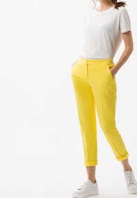 Pantalon jaune à coupe ajustée, avec deux poches latérales et ourlets retroussés, associé à un t-shirt blanc uni et des baskets blanches.