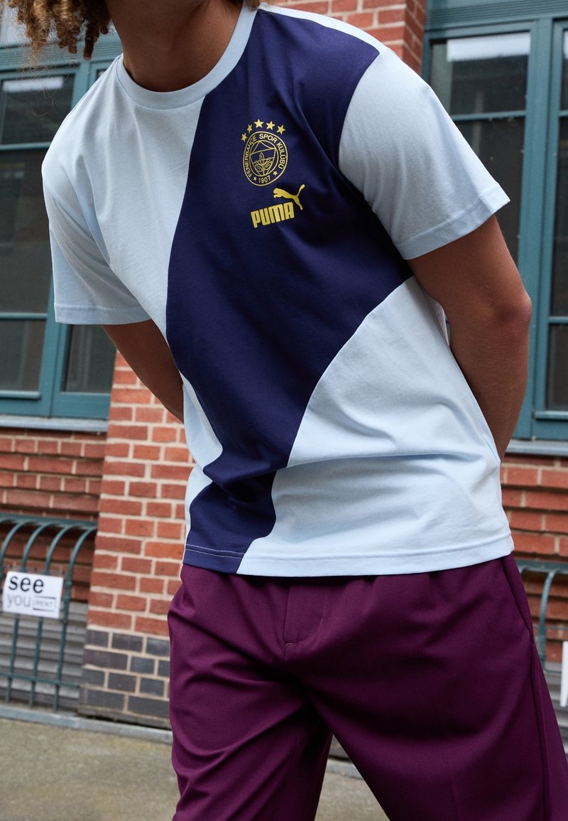 T-shirt Puma con pannelli azzurri e blu navy, con un logo raffigurante cinque stelle dorate. Tessuto in morbido cotone con design sportivo.