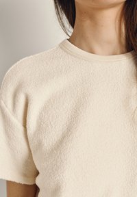 Roomkleurig shirt met korte mouwen van een zacht, gestructureerd stofje. Heeft een ronde halslijn en verlaagde schouders voor een ontspannen pasvorm.