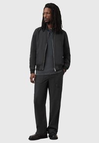 Czarna kurtka bombowa z zamek błyskawicznym z przodu, w połączeniu z ciemnoszarym swetrem i luźnymi czarnymi spodniami. Gładka tekstura i swobodny design.