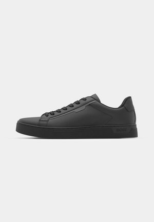 Black sneaker with smooth synthetic upper, round toe, flat laces, and a ribbed rubber sole. Minimalist design, featuring stitched accents.