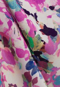 Tessuto floreale con motivi astratti colorati in rosa, blu, verde e nero su uno sfondo chiaro, con una texture morbida e un materiale leggero.