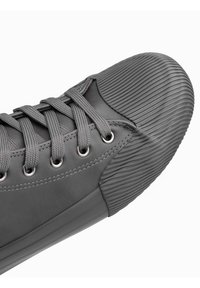 Zapatilla gris con parte superior de cuero liso, capucha de goma acanalada, ojales redondos y cordones planos, con un panel lateral texturizado.