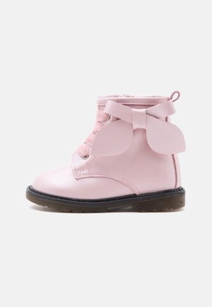 Bottine enfant rose avec semelle noire, lacets à l'avant et grand nœud décoratif sur le côté.